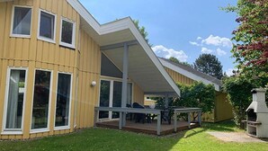 A two-story house with a covered patio, a barbecue area, and a large window overlooking the yard. - skandinavisches Ferienhaus in Mirow (Granzow)