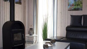 A modern living room with a black wood-burning stove, a white coffee table, a black leather sofa, and a painting on the wall. - skandinavisches Ferienhaus in Mirow (Granzow)