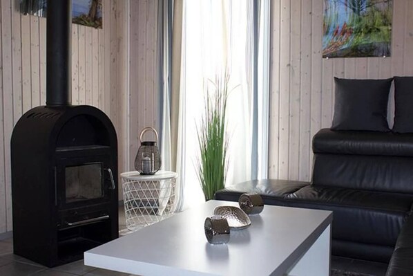 Un salon moderne avec un poêle à bois noir, une table basse blanche, un canapé en cuir noir et un tableau accroché au mur.