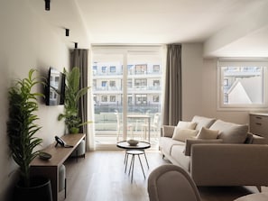 A modern living room with a sofa, a dining table, and a TV mounted on the wall. - Meral Units (Fuengirola)