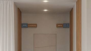 A hallway with a modern design, featuring a neutral color palette, two potted plants, and signs indicating a coworking space and an Aseos restaurant.