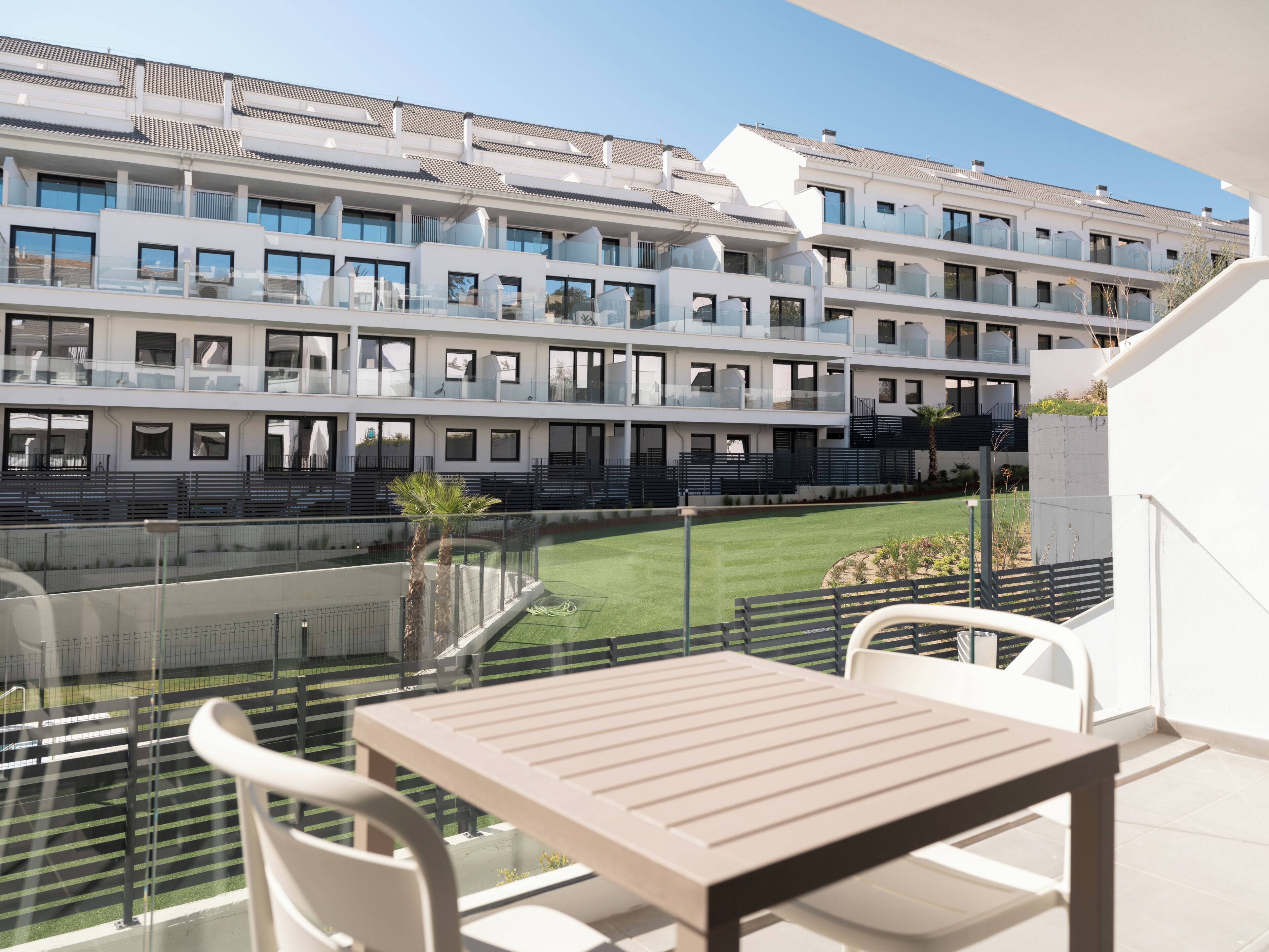 A balcony with a table and chairs, overlooking a pool and a building with multiple balconies.