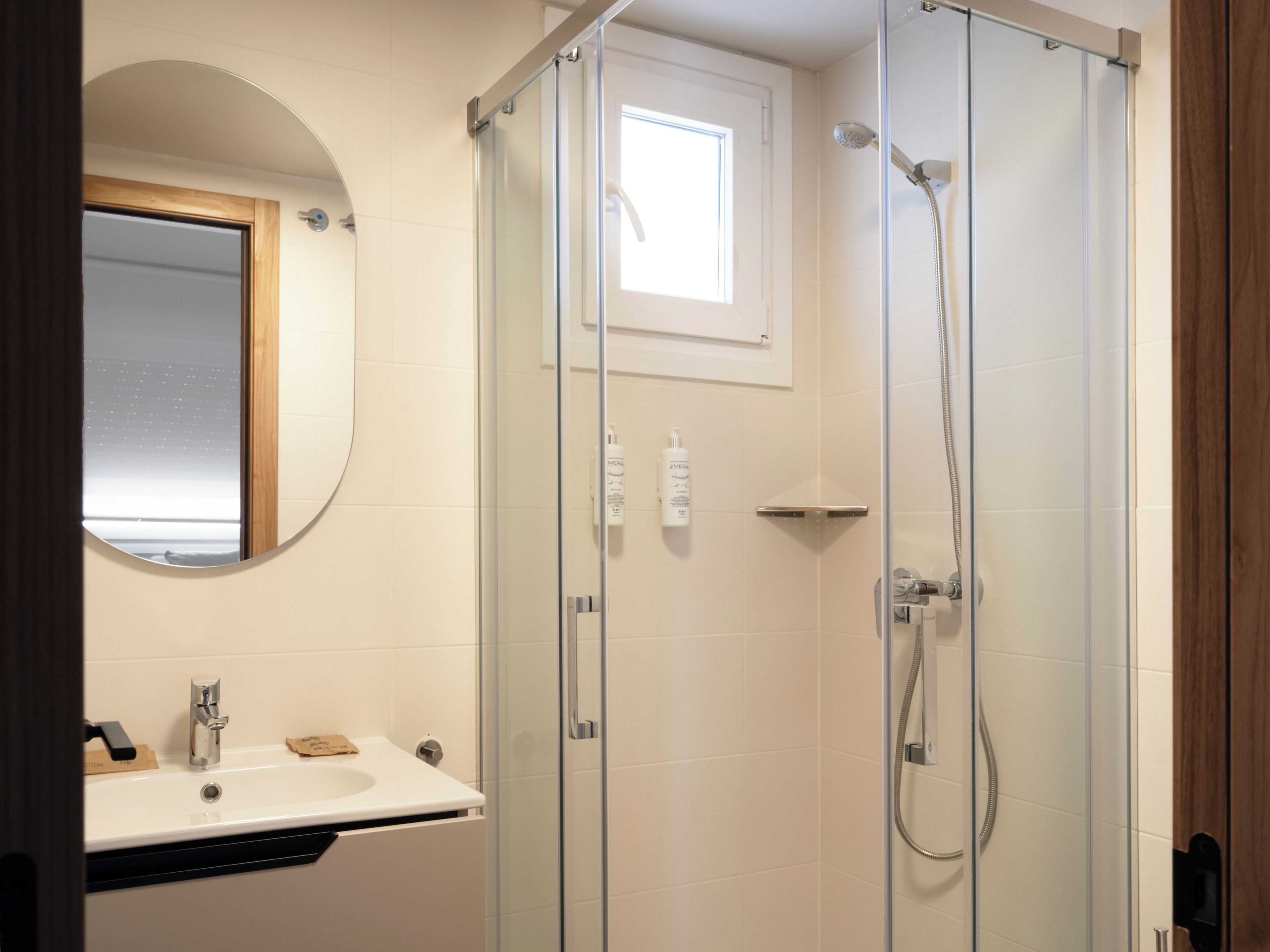 Un baño moderno con ducha cubierta por vidrio, lavamanos blanco y espejo.