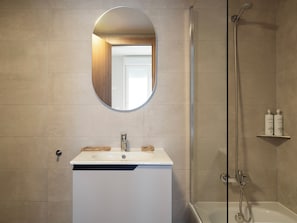 Ein Badezimmer mit weißem Waschbecken, einem Spiegel, einer Dusche und einem Ablagebereich für Toilettenartikel.