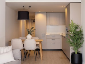 A modern kitchen with a dining area, featuring a wooden table, chairs, a vase with plants, and a potted plant.