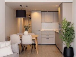 A modern kitchen with a dining area, featuring a wooden table, chairs, a vase with plants, and a potted plant.