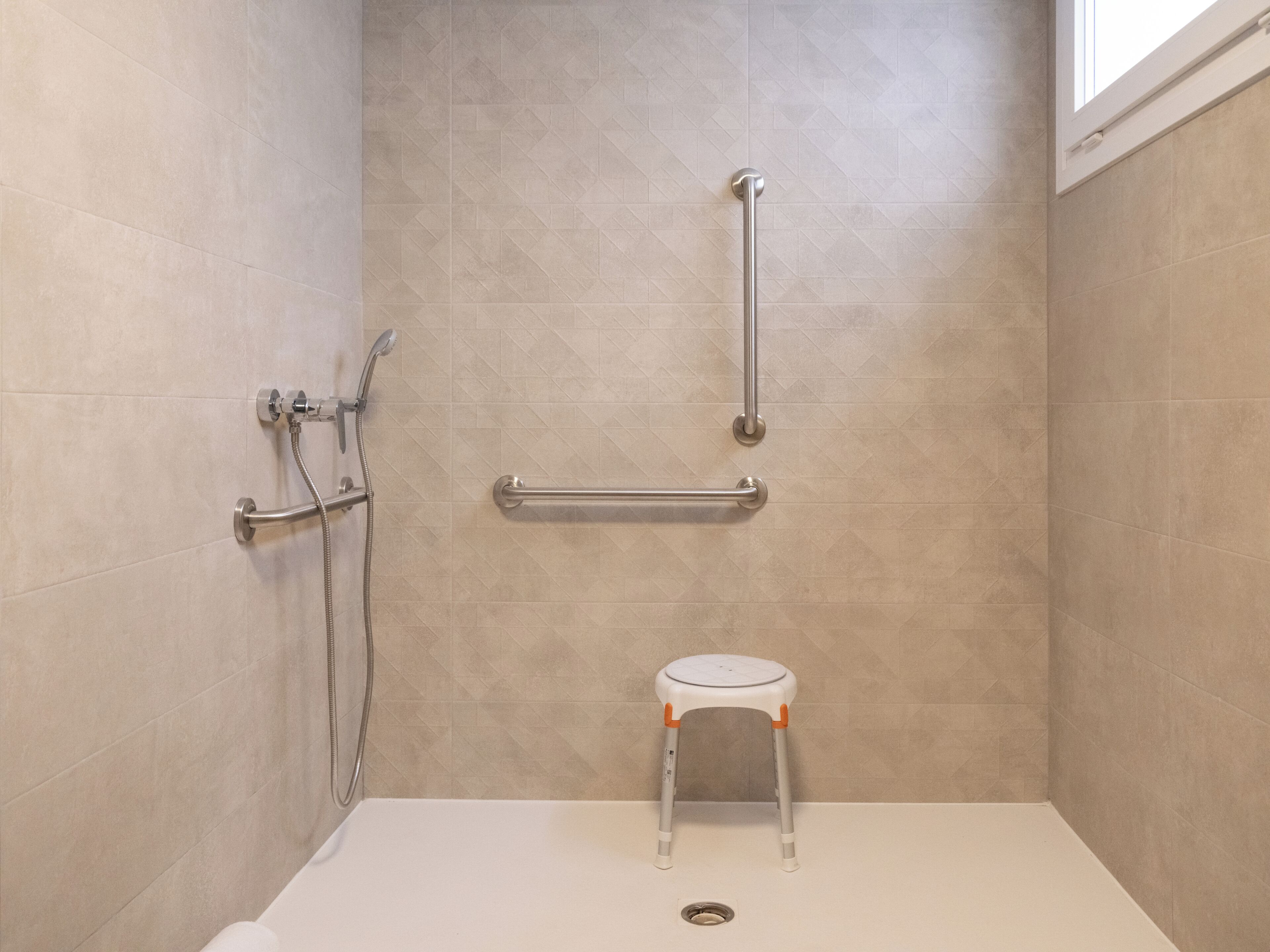 A shower with a grab bar, a handheld showerhead, and a step stool.