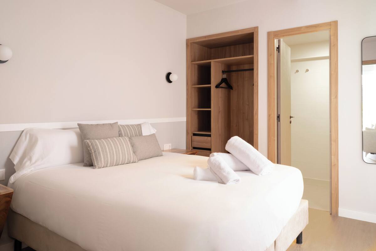 A neatly made bed with pillows, a wooden wardrobe, and a mirror on the wall.