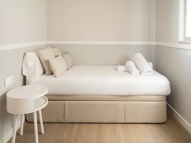 A small, single-bed room with a white bed, a small white table, and a window.