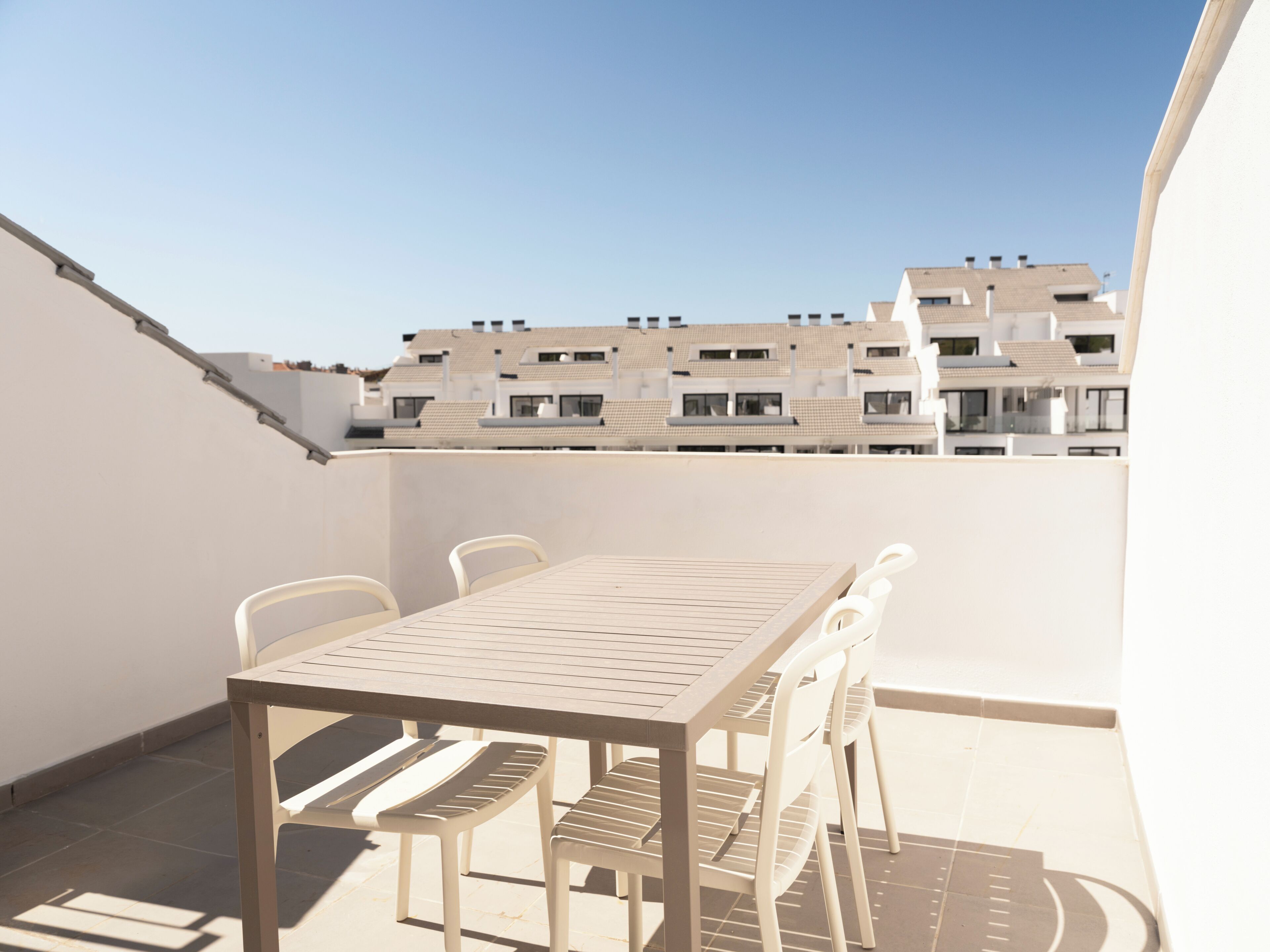 Een dakterras met een tafel en stoelen, en een uitzicht op woongebouwen in de verte.