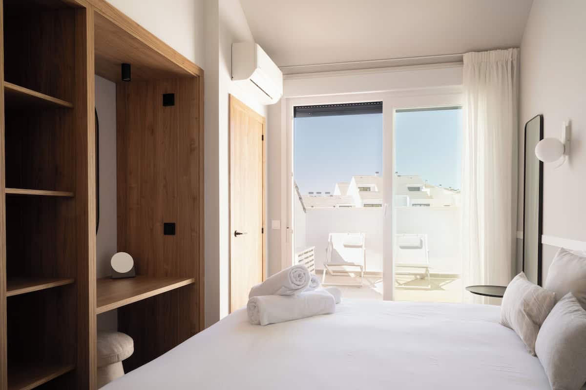 A hotel room with a large bed, wooden wardrobe, and a balcony with a view of buildings.