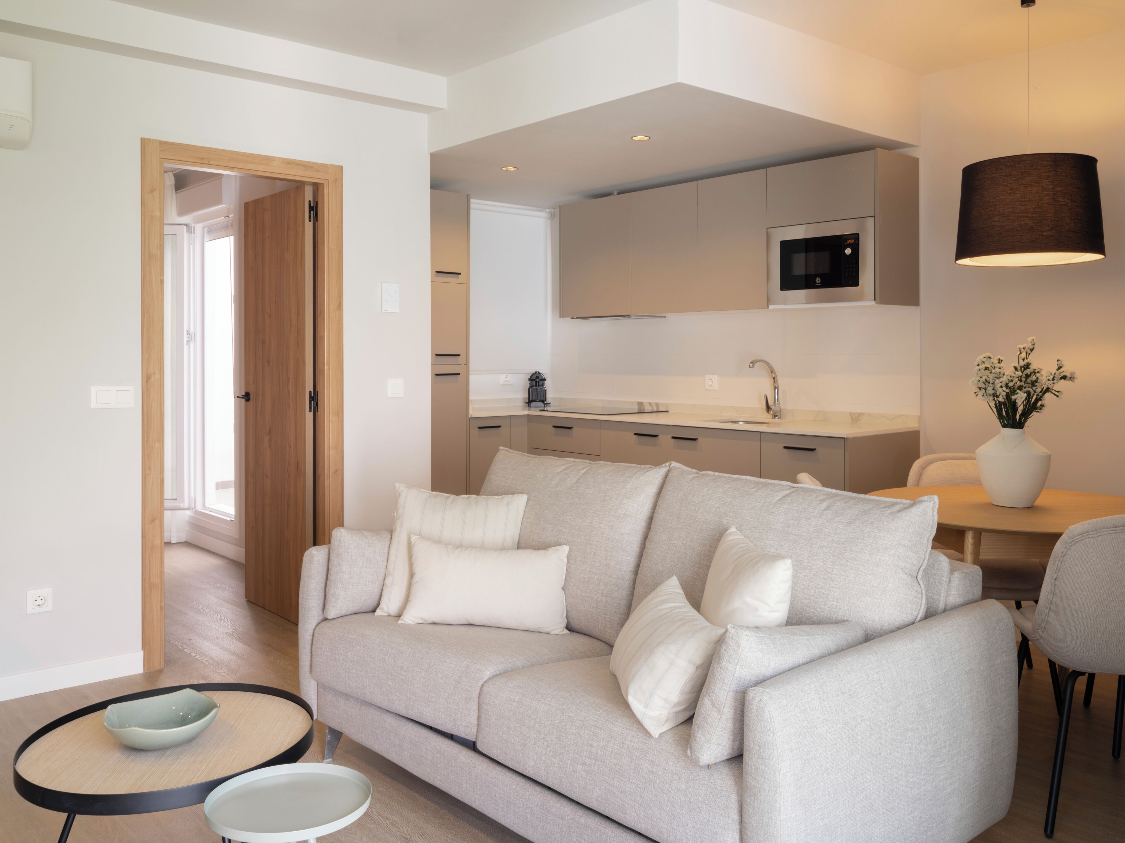 A modern living room with a sofa, a dining table, and a kitchen area in the background.