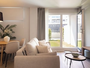 A modern living room with a sofa, a dining table, and a view of a building and greenery outside.