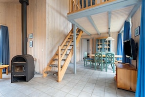 Cozy cabin-style interior with a central wood-burning stove, wooden staircase, and dining area.