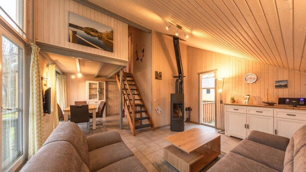 Una sala de estar acogedora con chimenea, muebles de madera y una escalera que sube a un nivel superior.