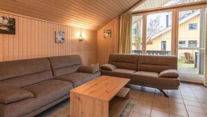 Una habitación acogedora con paredes de madera, un sofá marrón, una mesita de centro de madera y un ventanal con cortinas.