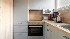 A compact kitchen with a built-in oven, microwave, and a coffee maker on the countertop. - Ferienhaus im skandinavischen Stil (Granzow)