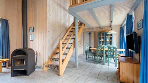 A wooden interior with a fireplace, staircase, dining area, and a television. - Ferienhaus im skandinavischen Stil (Granzow)