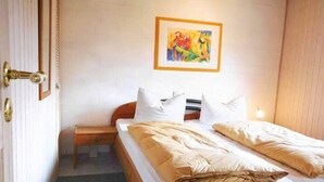 Une chambre avec un lit en bois, du linge de lit blanc, une petite table de chevet, un tableau encadré au mur et une porte avec une poignée en laiton.