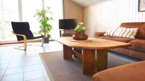 Un salon avec une table en bois, une chaise noire, un canapé marron et un téléviseur posé sur un meuble.