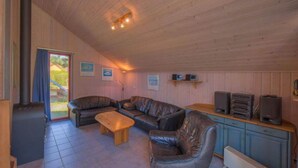 Una habitación acogedora con techo de madera, un sofá, una mesa de centro y un mueble con altavoces.