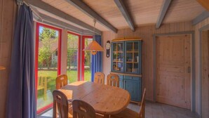 Un comedor de madera con una mesa, sillas, un armario y un ventanal con cortinas.