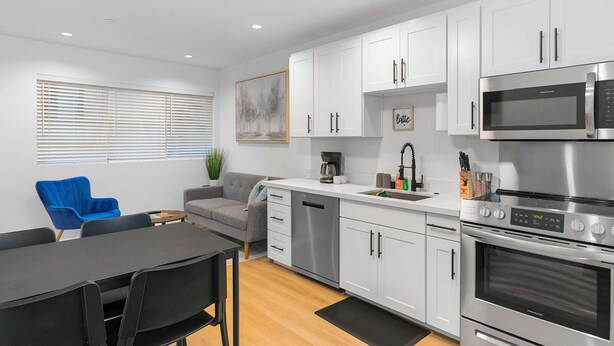 A modern kitchen with white cabinets, stainless steel appliances, a dining area with a black table and chairs, and a grey sofa. - The Cloudbreak Townhome - 88 Walkscore! (Seattle)
