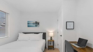 A hotel room with a bed, a desk with a laptop, a bedside table with a lamp, and a framed picture on the wall. - The Cloudbreak Townhome - 88 Walkscore! (Seattle)