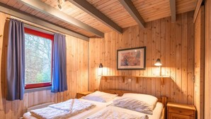 A wooden-paneled room with two beds, a window with curtains, a framed picture, and two wall-mounted lamps. - skandinavisches Ferienhaus in Mirow (Granzow)