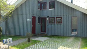 Een gebouw met twee verdiepingen, een rode deur, ramen, een schoorsteen en een parkeerbord.