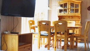 Un coin repas en bois avec un téléviseur fixé au mur, un buffet en bois doté de portes en verre et plusieurs chaises en bois.