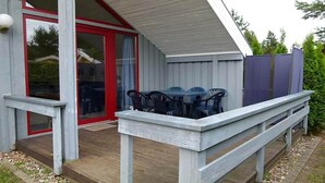 A covered outdoor area with a wooden deck, a table with chairs, and a red-framed glass door leading inside. - skandinavisches Ferienhaus in Mirow (Granzow)