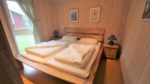 A wooden-paneled room with a double bed, two bedside tables with lamps, and framed pictures on the wall. - skandinavisches Ferienhaus in Mirow (Granzow)