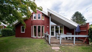 Et rødt træhus med en overdækket veranda og en lille terrasse.