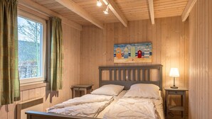 Et soveværelse med træpaneler, seng, to sengeborde, en lampe og et maleri af huse på væggen.