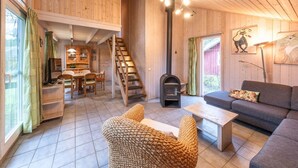 Et hyggeligt sommerhusinteriør med træpaneler, en pejs, en sofa og et spiseområde.