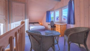 A cozy bedroom with a bed, a desk, and wicker chairs.
