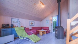 A cozy room with a wooden ceiling, a green reclining chair, a red sofa, a small table, and a fireplace.