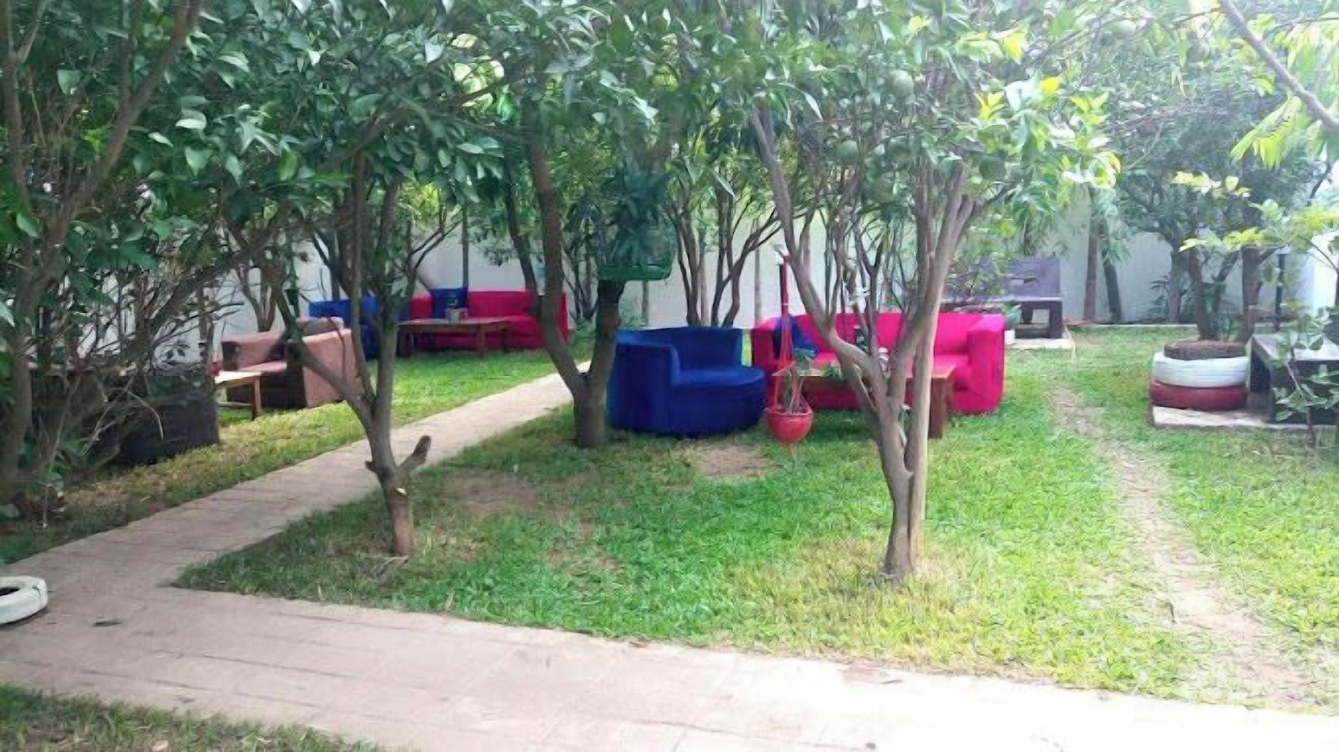 A garden with a paved walkway, green grass, and trees. There are outdoor seating areas with red and blue furniture.