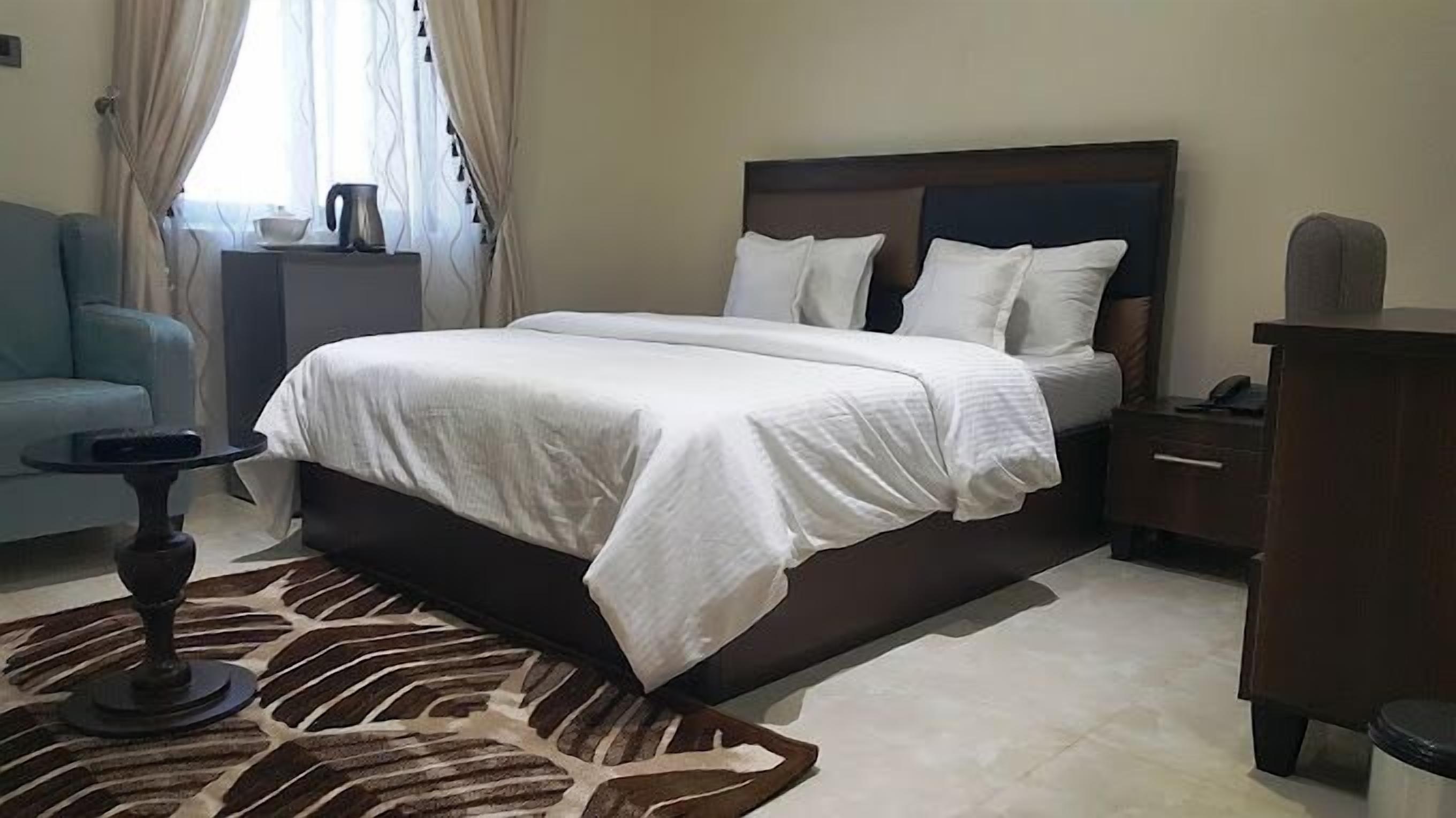 A bedroom with a large bed, a nightstand, a desk, a chair, and a patterned rug.