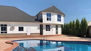 Una propiedad residencial con piscina, una casa de dos pisos y un jardín ajardinado.