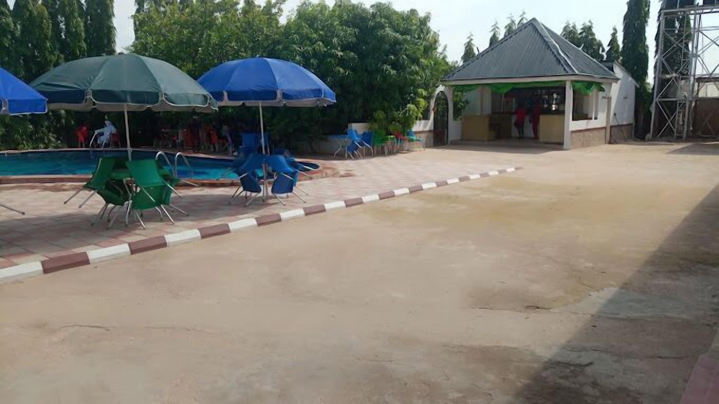A poolside area with chairs and umbrellas, a small pavilion, and a building with a sloped roof.