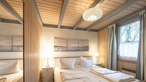 A double room with a wooden ceiling, two beds with white bedding, a chandelier, and a large window with curtains.