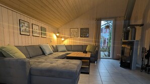 A cozy living room with a sectional sofa, a coffee table, and a fireplace. There are framed pictures on the wall and a window with curtains.