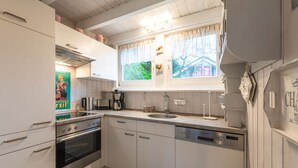A modern kitchen with white cabinetry, stainless steel appliances, a window with curtains, and a view of greenery outside.