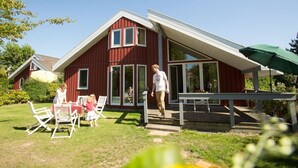 Une maison rouge avec un toit en pente, une véranda et un coin repas aménagé avec du mobilier d’extérieur.