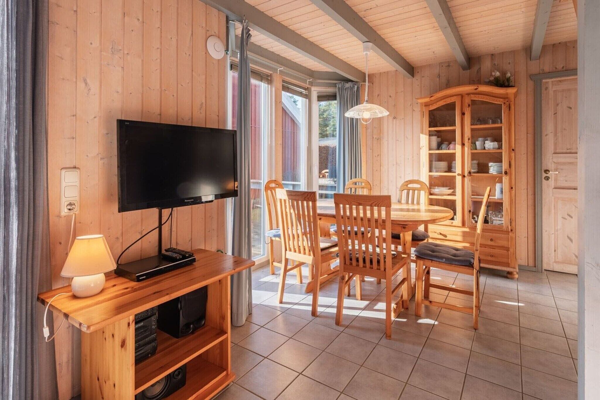 Een kamer met houten lambrisering, een televisie, eettafel, stoelen en een kast.