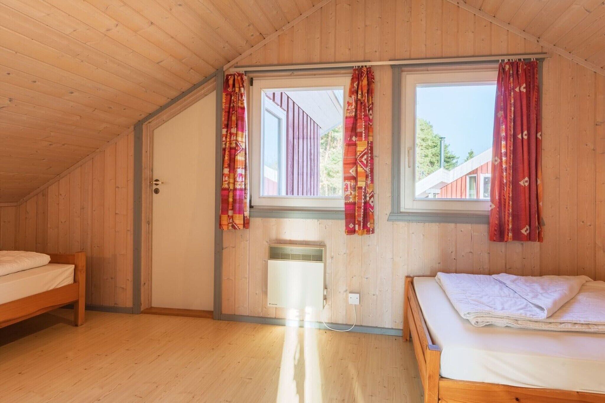 Una habitación con paredes de madera y techo inclinado, dos camas, una ventana con cortinas y un radiador.