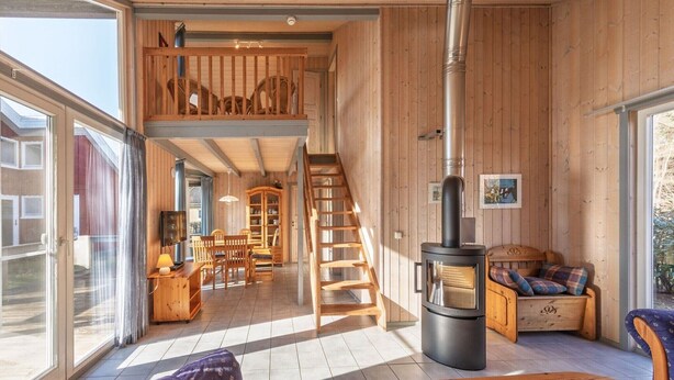 Un vaste espace de vie doté d’un intérieur en bois, d’une cheminée, d’un escalier menant à un niveau supérieur et d’une grande fenêtre laissant entrer la lumière naturelle.
