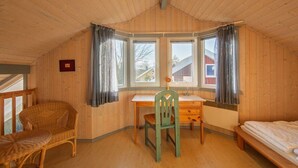 Une chambre confortable dans un chalet, avec un intérieur en bois, un bureau, une chaise, un lit et de grandes fenêtres dotées de rideaux.